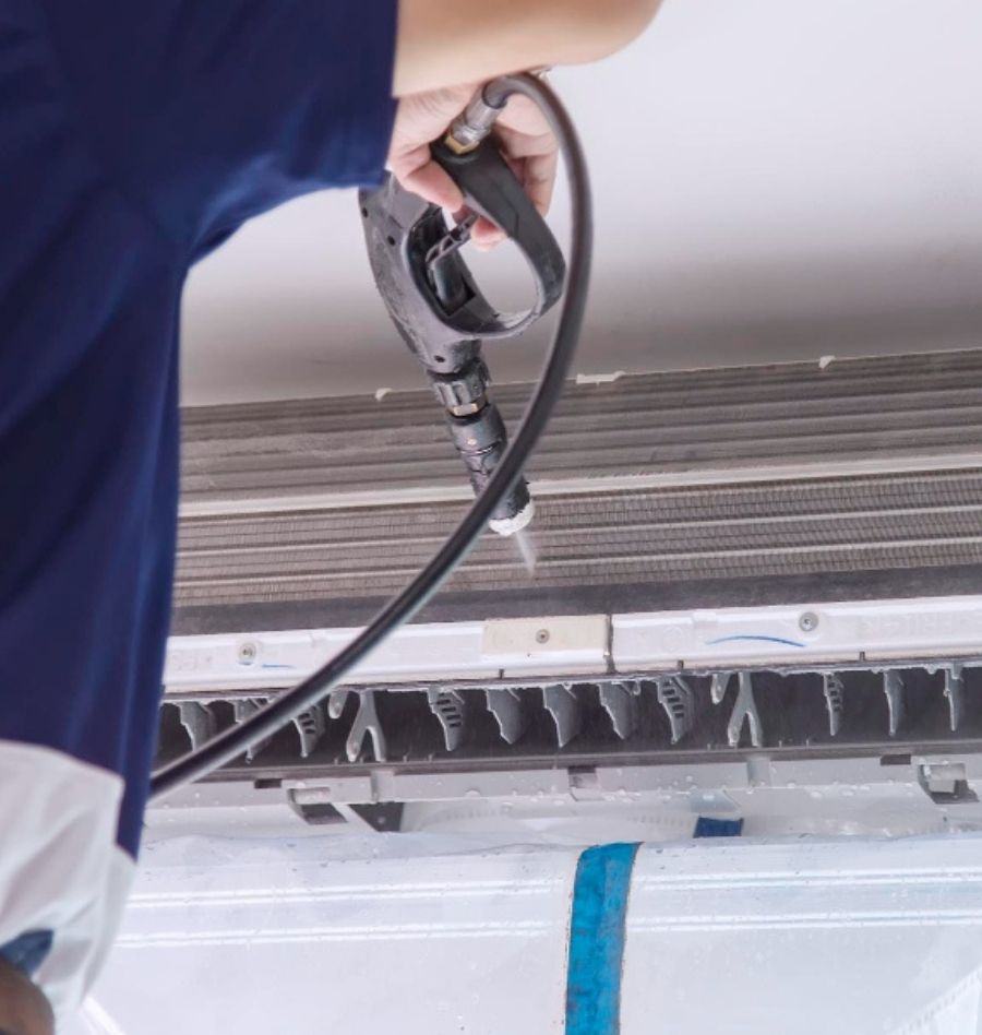 hand holding pressure washer pointed at indoor unit of a split type air conditioning